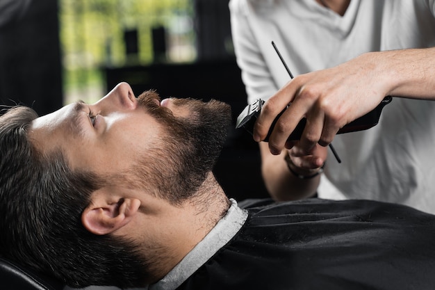 Aparar a barba com uma máquina de barbear. publicidade para barbearia e salão de beleza masculino.