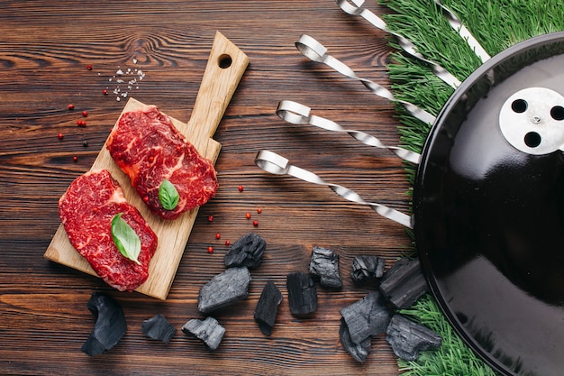 Foto aparato de barbacoa con filete crudo en tabla de cortar sobre mesa de madera