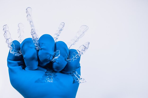 Los aparatos dentales invisibles se sostienen con una mano en un guante azul sobre un fondo blanco. Frenos de plástico retenedores de odontología para enderezar los dientes.