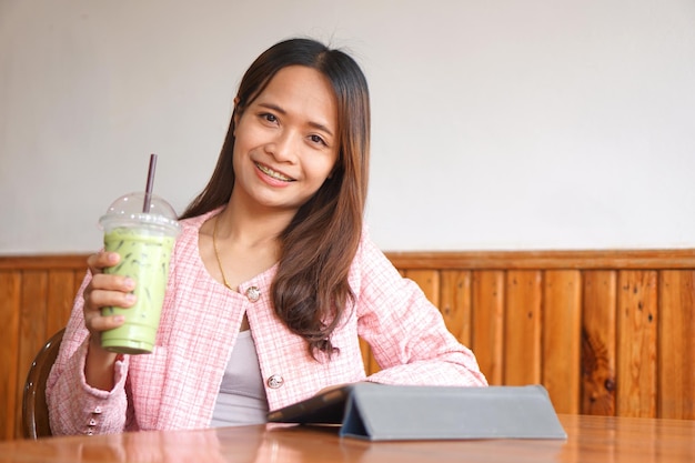 Aparelho de mulher asiática assiste computador Bebe chá verde para refrescar