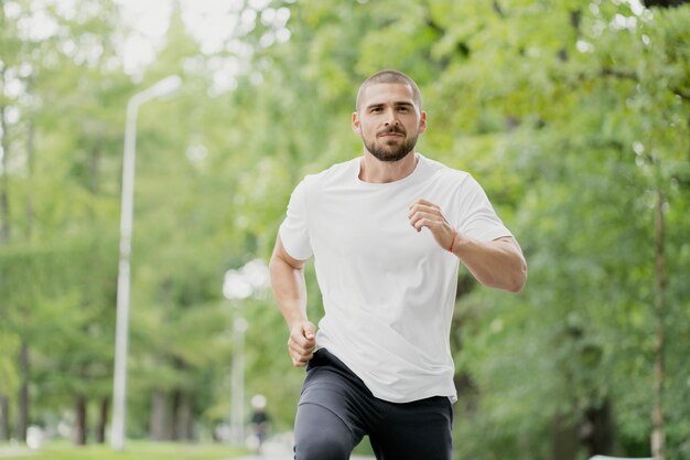 Aparência caucasiana de cabelos escuros de homem atlético correndo em um treinamento esportivo em esteira em um parque verde