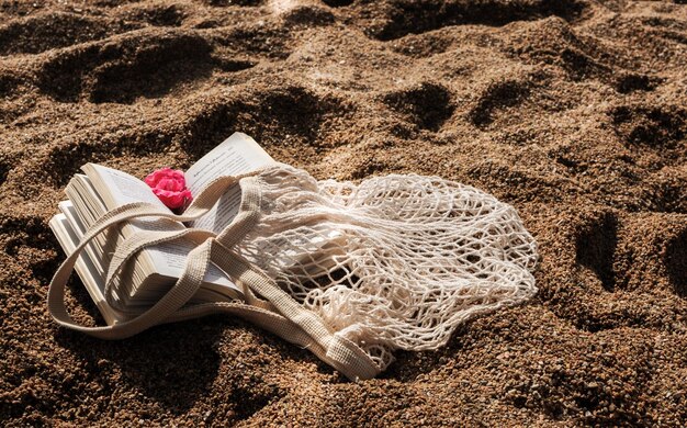 Apartamento de verão deitado em uma praia de areia saco de compras de malha ecológica e um livro