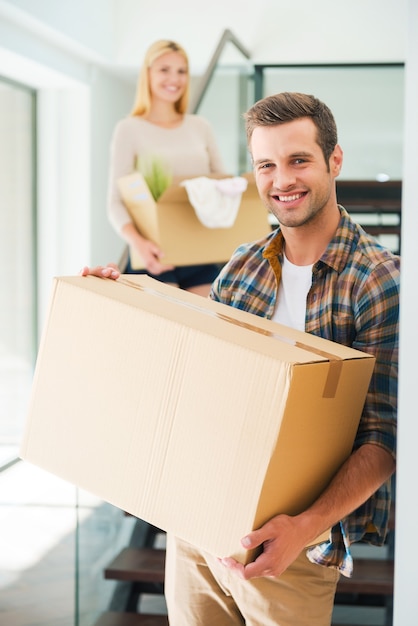 Foto apartamento nuevo para dos. pareja joven alegre sosteniendo cajas de cartón mientras está de pie en su nueva casa