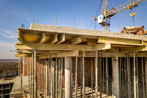 Foto apartamento ou prédio alto em construção, vista superior. paredes de tijolo, andaimes e pilares de suporte de concreto. guindaste de torre no espaço brilhante da cópia do céu azul. fotografia aérea de zangão.