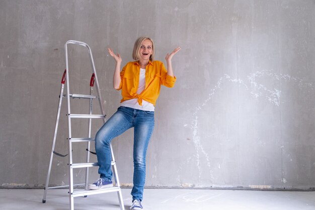 Apartamento de renovación feliz mujer sorprendida se sienta en las escaleras cerca de la pared vacía en casa reparaciones de pared gratis