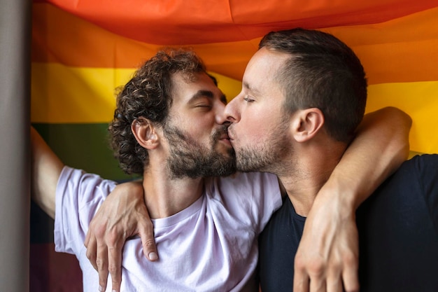 Foto apasionada pareja gay besándose con la bandera lgbtq en el fondo