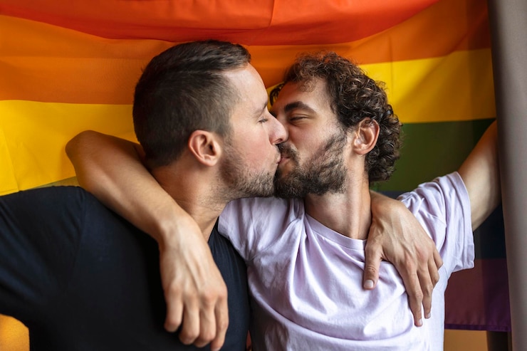 Foto apasionada pareja gay besándose con la bandera lgbtq en el fondo