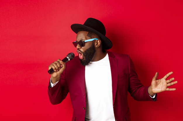 Apasionado cantante masculino negro actuando en rojo, cantando en el micrófono en rojo