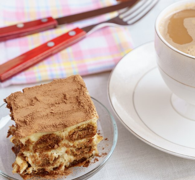 Foto apelmace el tiramisu en una placa con una taza de té en fondo.