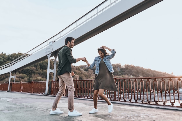 Apenas dance! Comprimento total do lindo jovem casal de mãos dadas e girando