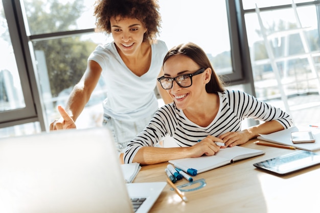 Foto apenas dê uma olhada. mulheres jovens sorrindo alegres usando seus laptops e sentando-se à mesa enquanto se arrumam para as aulas