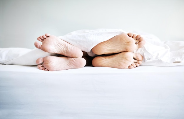 Apenas relaxe Foto de um casal com os pés descalços saindo debaixo dos lençóis em casa