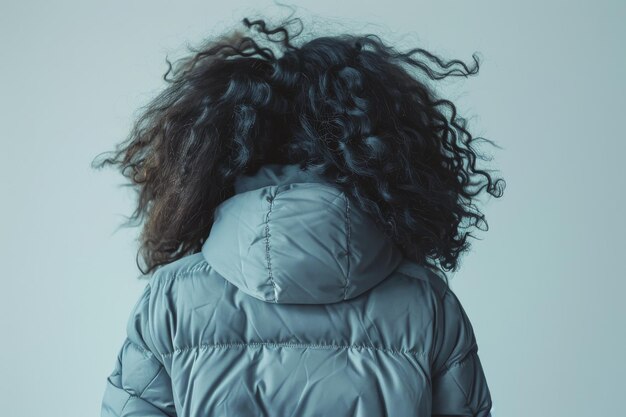 Apenas uma mulher com cabelos rizados pretos em uma jaqueta de inverno azul em um fundo azul vista de trás