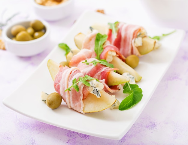 Aperitif mit Birne, Blauschimmelkäse, Prosciutto Schinken und Toast für Feiertage auf einer weißen Platte.