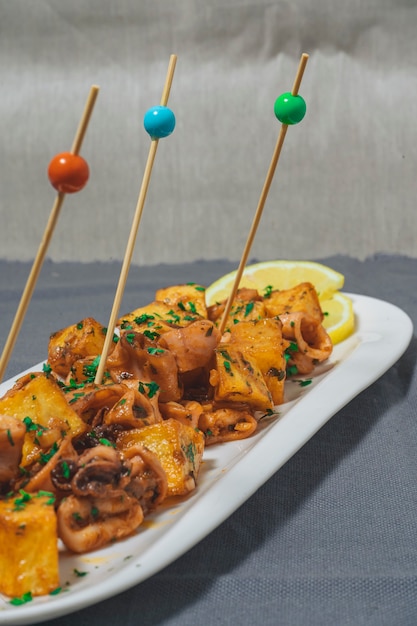 Aperitif oder typisch spanischer Tapa-Baby-Tintenfisch mit Knoblauch und Kartoffeln, serviert auf einem länglichen Weiß