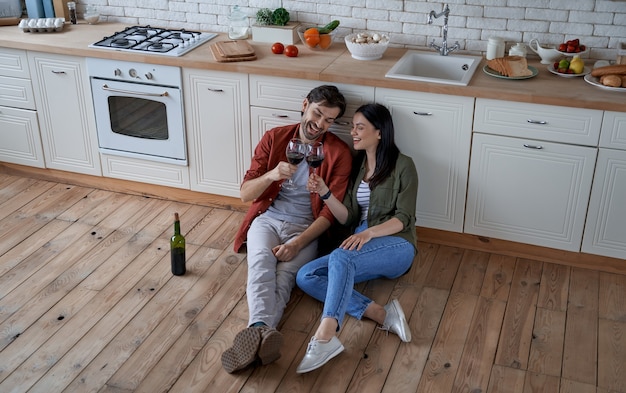 Aperitif-Zeit in voller Länge von jungen schönen Paaren, die in der modernen Küche auf dem Boden sitzen