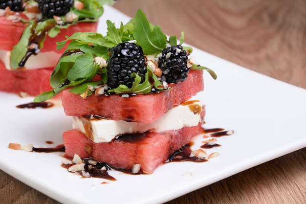 Aperitivo apilado rodajas de sandía, queso feta, rúcula, salsa de moras y nueces