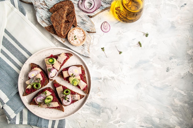 Aperitivo de arenque o concepto de comida rápida sándwich smorrebrod tradicional Sándwiches de arenque con pan de centeno ensalada de remolacha pepino fresco y aros de cebolla vista superior