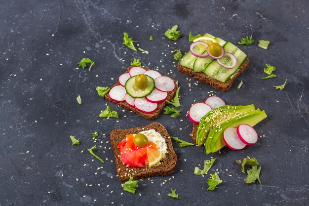 Aperitivo, bocadillo abierto con diferentes ingredientes: salmón y verduras (aguacate, pepino, rábano). Alimentación saludable. Comida orgánica y vegetariana. De cerca,