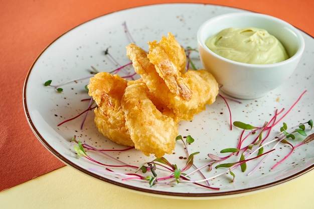 Aperitivo - camarones fritos en tempura con salsa en un plato blanco sobre superficie coloreada. Comida para los dedos, pub