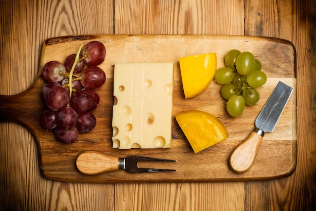 Aperitivo com queijo e uvas em uma placa de madeira em uma vista superior