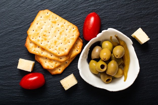 Aperitivo de la comida Aceitunas queso, tomates y galletas en un tablero de pizarra negro