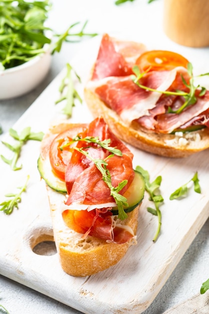 Aperitivo crostini sándwiches abiertos con queso crema, jamón, pepino y rúcula en la mesa blanca Vista superior con espacio para copiar