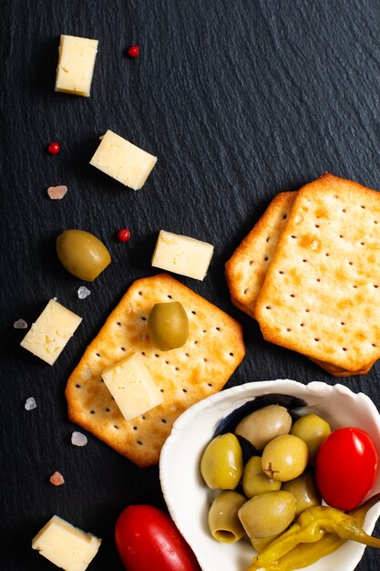 Aperitivo de alimentos azeitonas queijo, tomate e bolacha na placa de ardósia preta