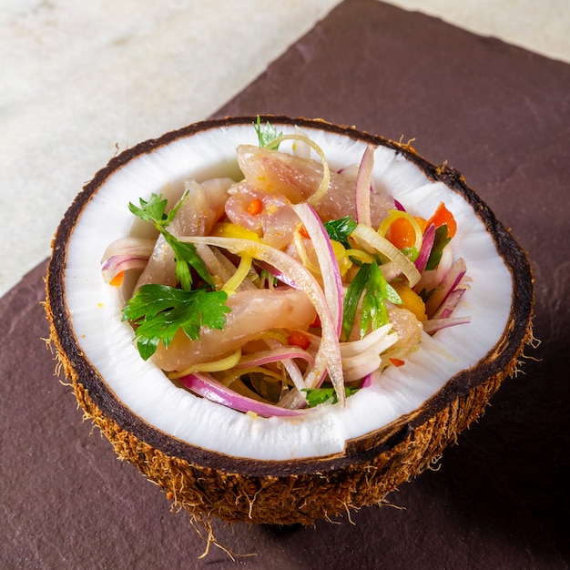 aperitivo de peixe fresco marinado em frutas cítricas com frutas tropicais servido em uma tigela de coco.