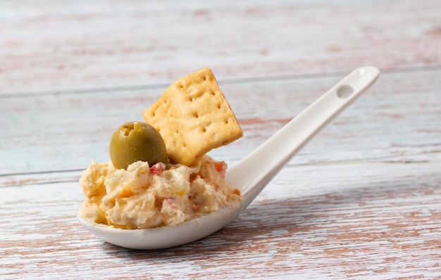 Aperitivo de salada russa em uma colher de cerâmica em um fundo de madeira