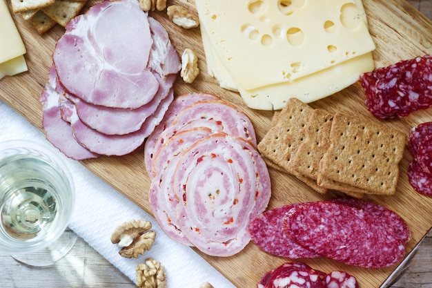 Aperitivo de vários tipos de salsichas, carnes, queijos e bolachas numa tábua de madeira, servido ao vinho.