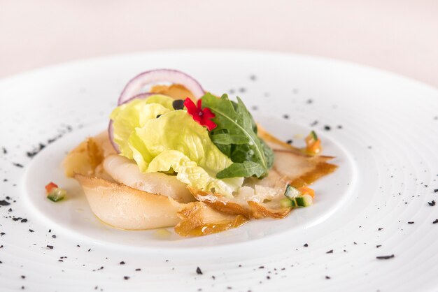 Aperitivo fresco con pescado blanco ahumado, rúcula, espinaca y ensalada verde, con flores rojas