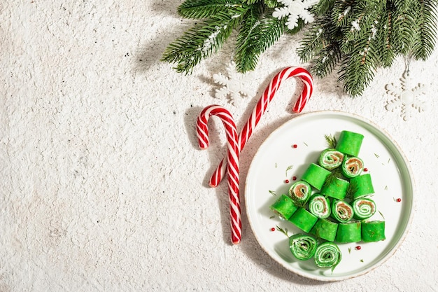 Aperitivo frío, decorado en forma de árbol de Navidad. Crepes finas, queso crema, salmón ligeramente salado, verduras, luz dura de moda, sombra oscura. Decoración festiva de año nuevo, fondo de masilla, vista superior