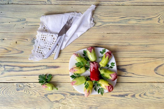 Aperitivo frío con tocino de pimientos verdes y salchichas en forma de flores en un primer plano de la mesa de madera