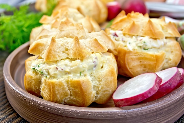 Aperitivo de huevos de eneldo de rábano y queso en profiteroles en un plato de arcilla eneldo sobre un fondo de tablas de madera