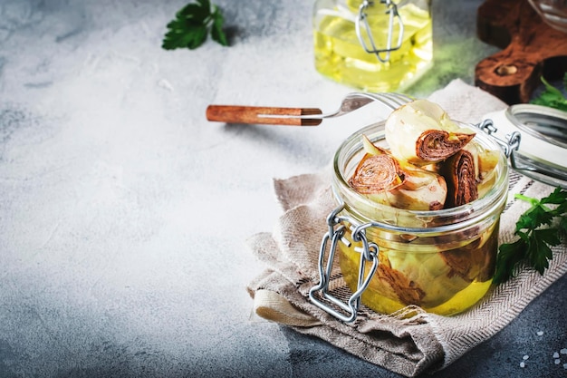 Aperitivo italiano Alcachofas enlatadas en aceite de oliva en frasco de vidrio con limón y hierbas sobre fondo de mesa de cocina gris espacio de copia enfoque selectivo