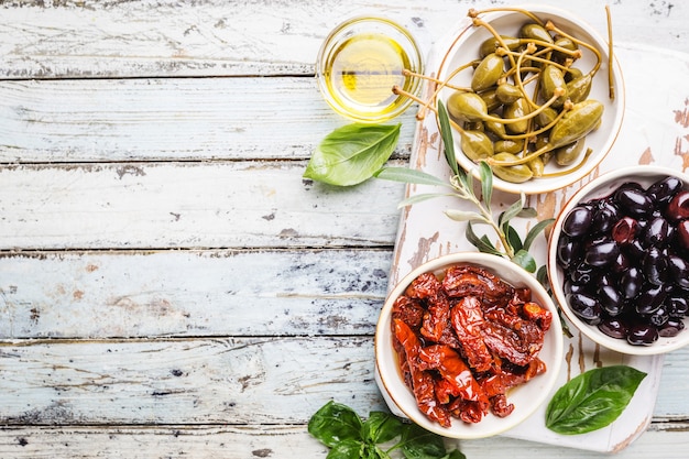 Aperitivo italiano desde arriba. Surtido de snacks mediterráneos. Vista superior de aceitunas negras, alcaparras, aceite de oliva y tomates secados al sol.