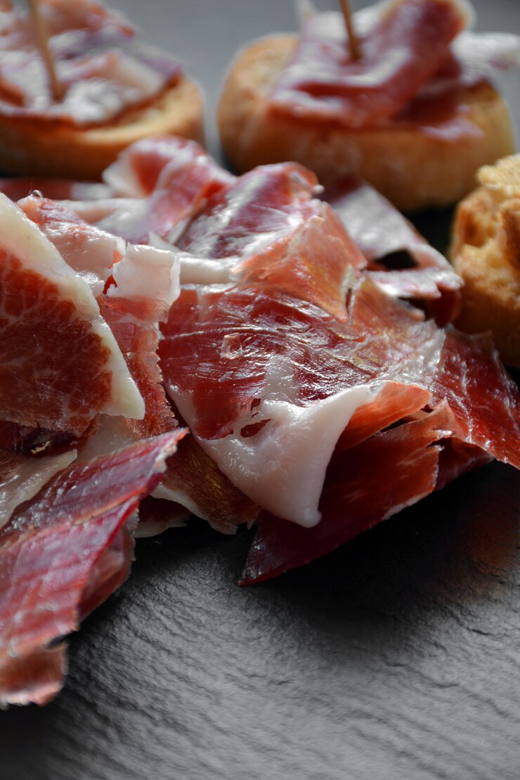 Foto aperitivo de jamón serrano con pan asado y acompañado de una copa de vino.