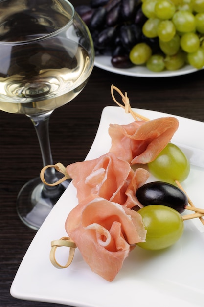 Aperitivo de jamón y uvas en un pincho con una copa de vino blanco