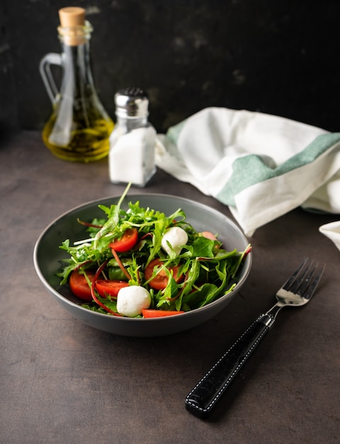 Aperitivo ligero. ensalada verde fresca con hojas de lechuga y rúcula. con tomates cherry y queso mozzarella. bajo perfil, humor oscuro, espacio de copia.