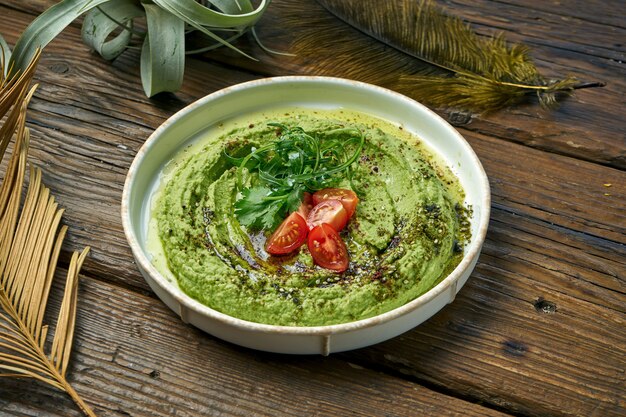 Aperitivo oriental clássico - hummus de abacate com verduras e tomate cereja em um prato branco sobre uma mesa de madeira