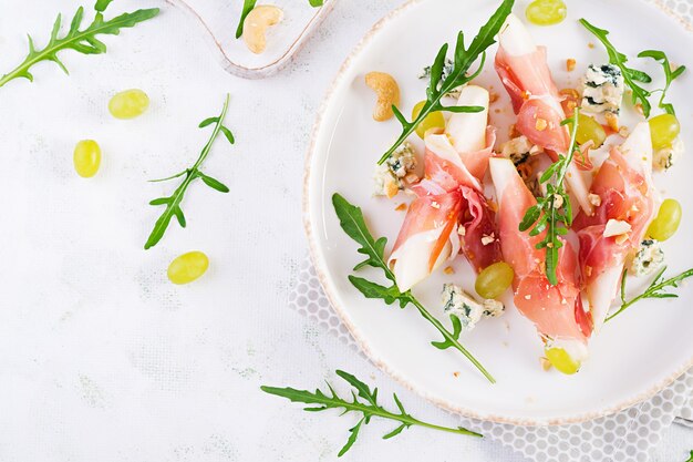 Aperitivo con pera, queso azul y jamón prosciutto para vacaciones en un plato blanco. Vista superior, endecha plana