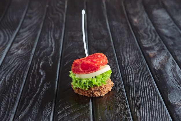 Aperitivo para la recepción. Sándwich pequeño con salchicha, sheese y ensalada de hojas en brocheta