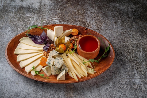 Un aperitivo en un restaurante, un surtido de quesos. Rebanadas de queso en capas sobre un plato con verduras contra una mesa de piedra gris