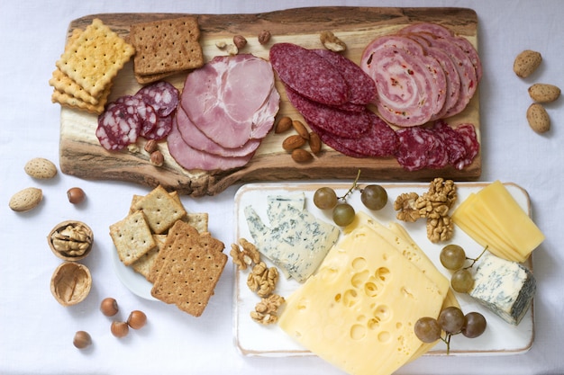 Aperitivo de varios tipos de salchichas, carnes, quesos y galletas en una tabla de madera, servido al vino.