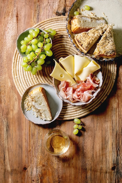 Aperitivos antipasti con focaccia siciliana blanca. Tarta de pan tradicional con cebolla servida con jamón prosciutto, queso, uvas y copa de vino blanco