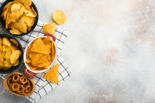 Aperitivos Comida poco saludable Todos los bocadillos clásicos de patata con palomitas de maíz y aros de cebolla y pretzels salados en platos de cuenco sobre fondo de hormigón gris Comida poco saludable para los dientes de la piel del corazón de la figura