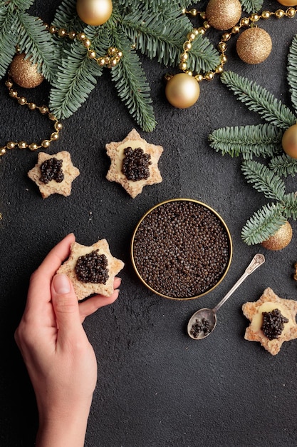 Aperitivos de caviar preto estrelam na mão de um humano em uma mesa preta decorada de natal