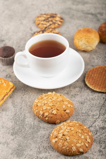 Aperitivos dulces con taza de té blanco colocado sobre una mesa de piedra.