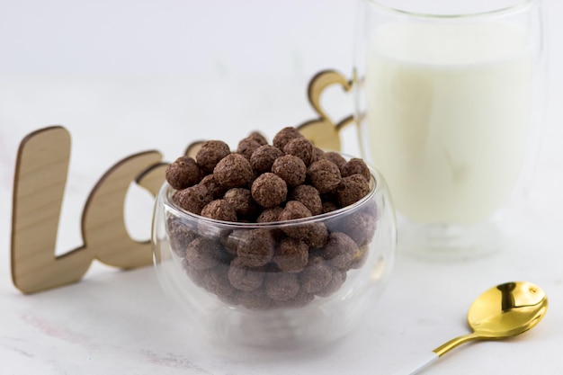 Aperitivos en forma de bolas de chocolate Un bol con un desayuno rápido un vaso de leche y la inscripción amor sobre un fondo de mármol blanco